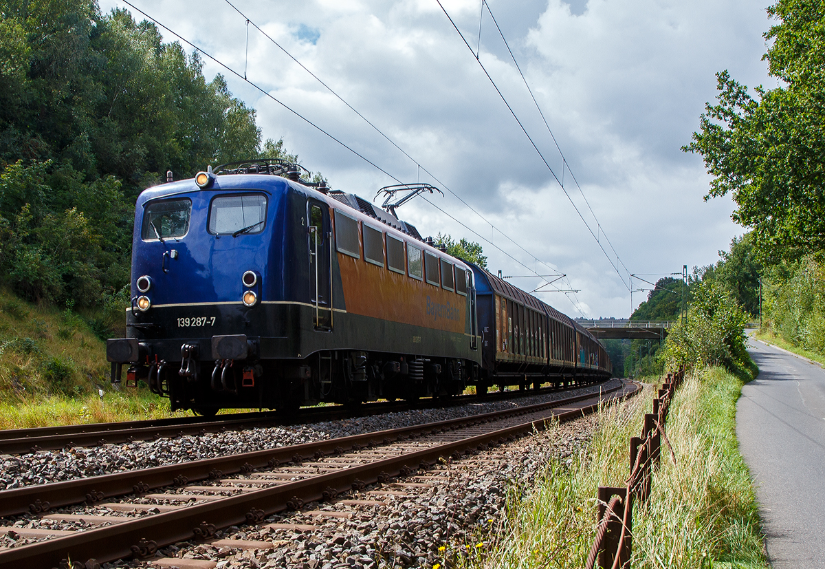 Die 139 287-7 (91 80 6139 287-7 D-BYB) der BayernBahn GmbH fährt am 26.08.2021 mit dem sogenannten  Henkelzug  (Langenfeld/Rhld. nach Gunzenhausen), bei Wissen (Sieg) über die Siegstrecke (KBS 460) in Richtung Siegen.

Die Lok wurde 1963 von Krauss-Maffei AG in München-Allach unter der Fabriknummer 18956 gebaut, er elektrische Teil ist von den Siemens-Schuckert-Werke (SSW) in Berlin. Als DB E10 287 wurde in Dienst gesetzt, mit der Einführung des EDV-Nummernsystems wurde sie zum 01.01.1968 zur DB 110 287–0. Die Lok ist mit Einholmstromabnehmern ausgerüstet, sie ist die letzte gebaute Kasten 110er. Zur 139er wurde sie erst 1994 nach einem Umbau, der Lokkasten wurde auf Drehgestelle der Baureihe 140 (E40) gesetzt und es folgte die Umzeichnung in DB 139 287-7. Zum Mai 2009 erfolgte die Z-Stellung bei der DB AG.

Zum 1.Oktober 2011 wurde die Lok durch die BayernBahn GmbH erworben und erhielt anschließend eine Untersuchung. Die Neulackierung in kobalt-blau/orange erhielt sie dann 2017. 