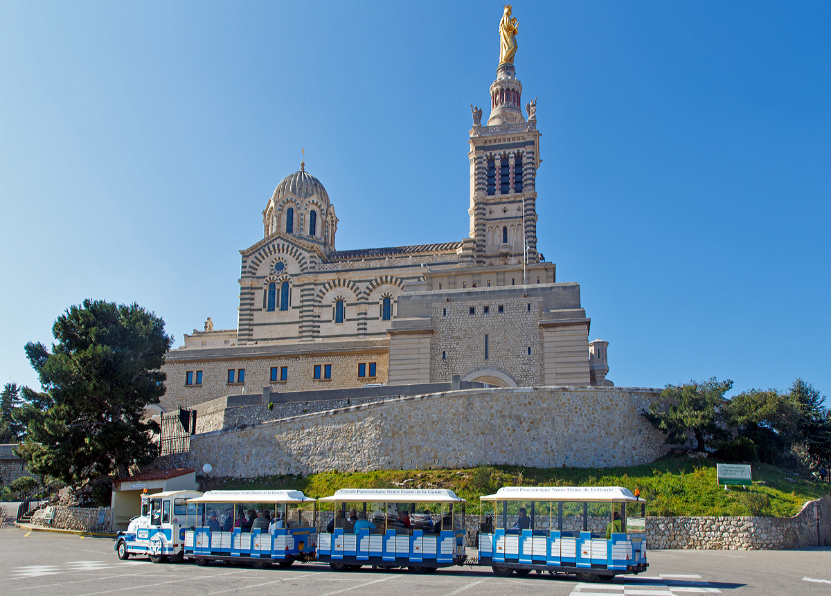 
Ein Petit Train (ein Muson River 1894 vom italienischen Hersteller DOTTO TRAINS mit 3 Anhänger) steht zu Füssen der Marien-Wallfahrtskirche Notre-Dame de la Garde in Marseille am 26.03.2015. Mit dem Petit Train kann man für 8 Euro vom alten Hafen (Vieux Port) auf die höchste Erhebung (161 m) von Marseille fahren. 

Von hier oben hat man dann eine wundervolle Aussicht auf Marseille und auf die Frioul-Inseln. 

Die Wallfahrtskirche Notre-Dame de la Garde, im Volksmund La Bonne Mère – „die gute Mutter“. Sie wird jährlich von zwei Millionen Menschen besucht. Das neuromanisch-byzantinische Gotteshaus wurde an der Stelle einer mittelalterlichen Kapelle ab 1853 nach Plänen von Henri-Jacques Espérandieu erbaut und am 4. Juni 1864 durch den Kurienkardinal Clément Villecourt geweiht. 1879 erhielt sie den Rang einer Basilica minor.
