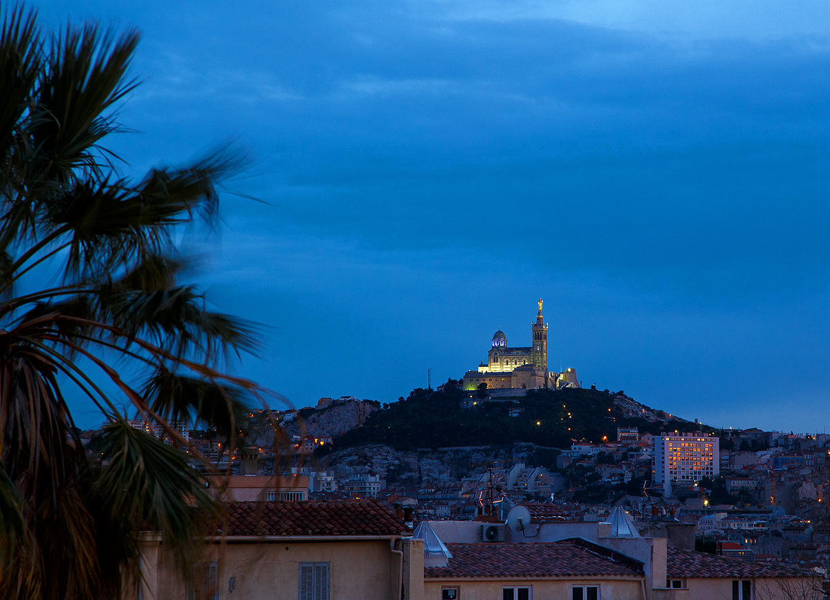 Leider nicht „über den Dächern von Nizza“, aber von Marseille.....
Ein Blick vom Vorplatz am Bahnhof Marseille St-Charles am Abend des 25.03.2015 über die Dächer hinweg auf die Marien-Wallfahrtskirche Notre-Dame de la Garde.

Die Wallfahrtskirche Notre-Dame de la Garde, im Volksmund La Bonne Mère – „die gute Mutter“. Sie wird jährlich von zwei Millionen Menschen besucht. Das neuromanisch-byzantinische Gotteshaus wurde an der Stelle einer mittelalterlichen Kapelle ab 1853 nach Plänen von Henri-Jacques Espérandieu erbaut und am 4. Juni 1864 durch den Kurienkardinal Clément Villecourt geweiht. 
