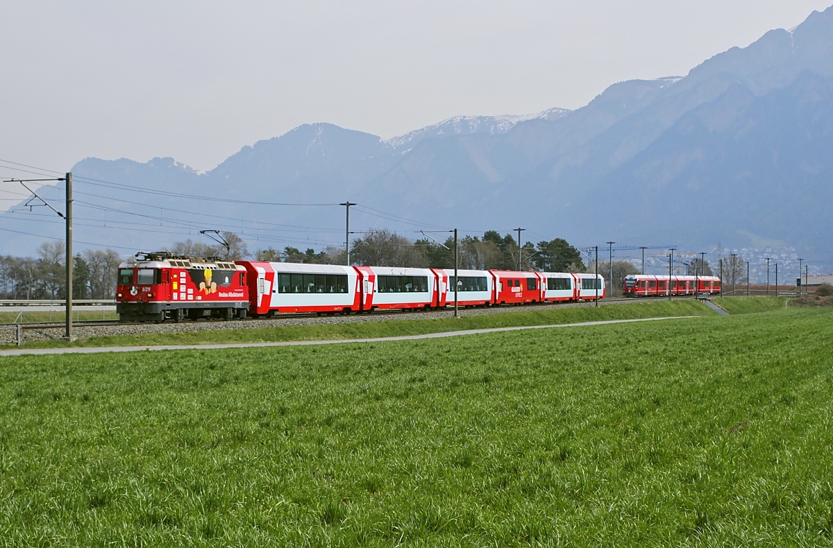 Nochmals der Glacier-Express am 29.03.2022 bei Felsberg, diesmal mit der Ge 4/4 II 629  Tiefenkastel  aus Chur kommend. Die Lok wirbt für den Neubau des Albulatunnels.