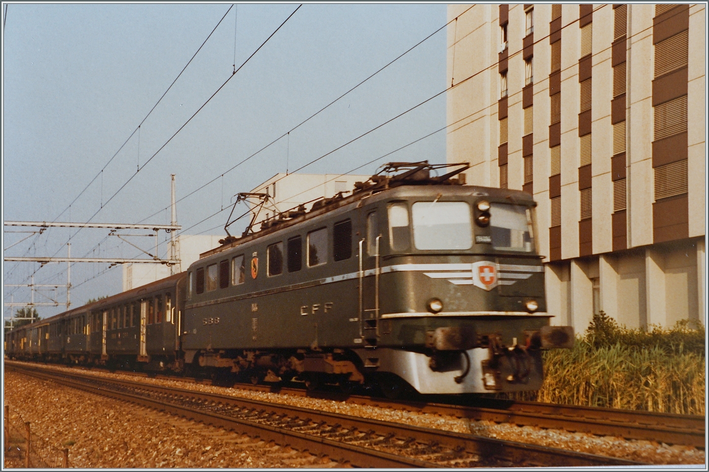 Die SBB Ae 6/6 11414  Kanton Bern  (und Vorbild der klassischen Märklin Ae 6/6) ist zwischen Lengnau und Grenchen Süd mit einem Personenzug unterwegs. 

Analogbild vom 20 Juli 1984 