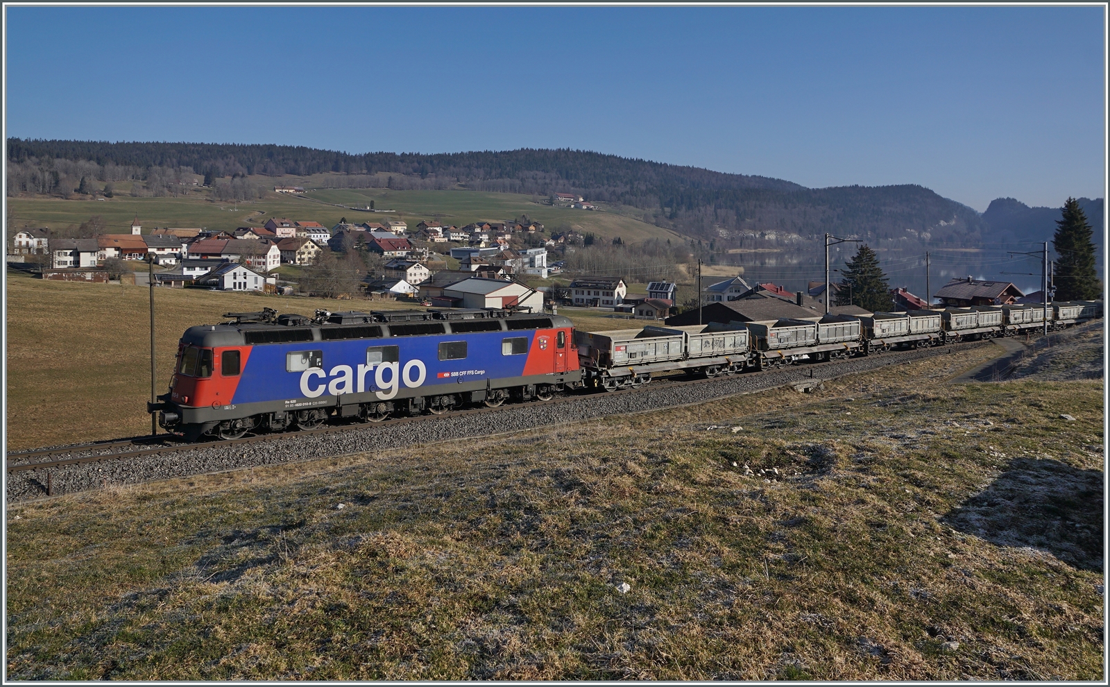 Die SBB Re 6/6 11610 (Re 620 010-9)  Spreitenbach  bringt etliche leere Fans-u Wagen als G�terzug 69701 von Lausanne-Triage nach Le Brassus und konnte hier bei Les Charbonni�res mit dem Hintergrund des Lac de Brenet fotografiert werden. 24. M�rz 2022